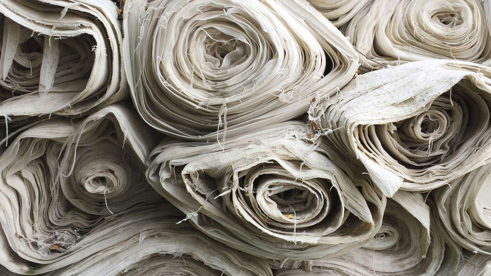 Rolls of undyed fabric packed tightly in storage, representing imported inputs held under bond for export production