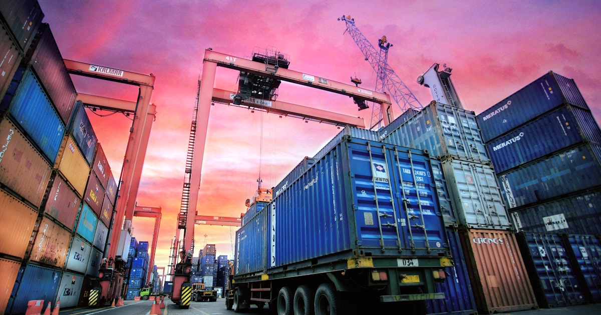 Shipping containers stacked at a busy port under a dramatic sunset sky, representing the cargo risk that insurance is designed to cover