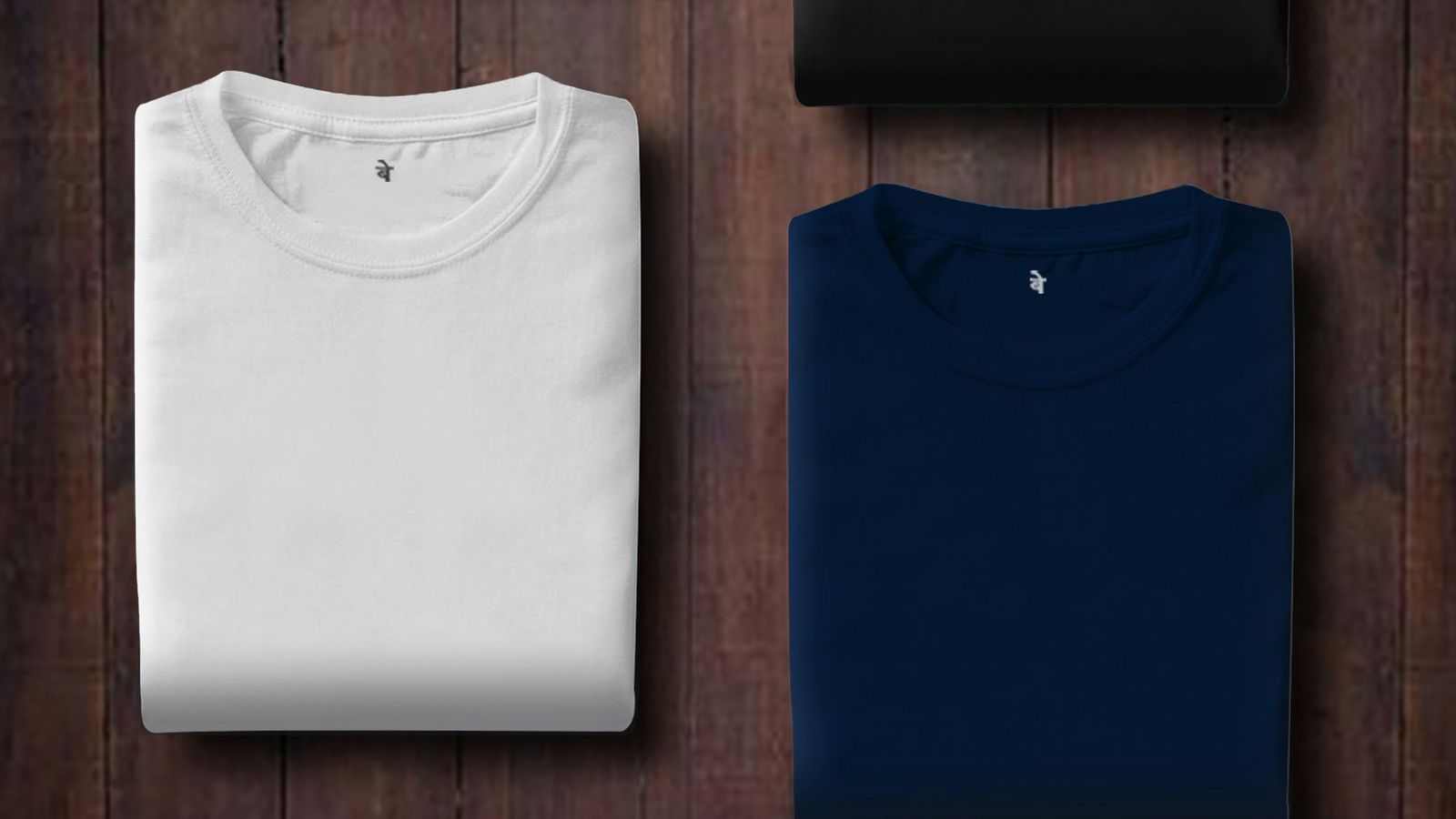 Plain folded t-shirts in white, navy and black laid on a wooden surface, representing unbranded goods carrying no third-party logos
