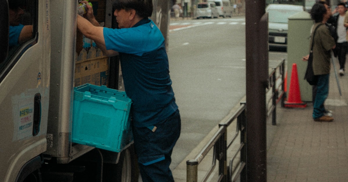 Worker loading a crate into a delivery truck on a city street, representing last-mile delivery to Dhaka