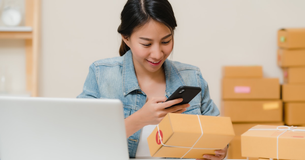 Small business owner checking a package next to a laptop and boxes, representing importing in small quantities for small businesses