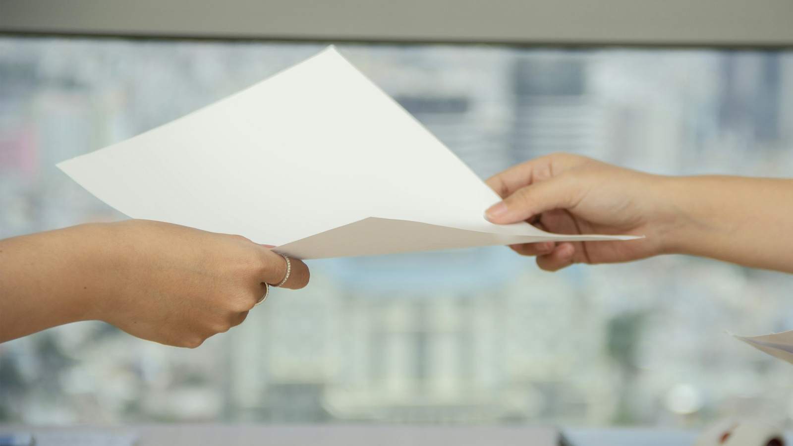 Two hands passing a single sheet of paper between them in an office, representing the proforma invoice that starts an import