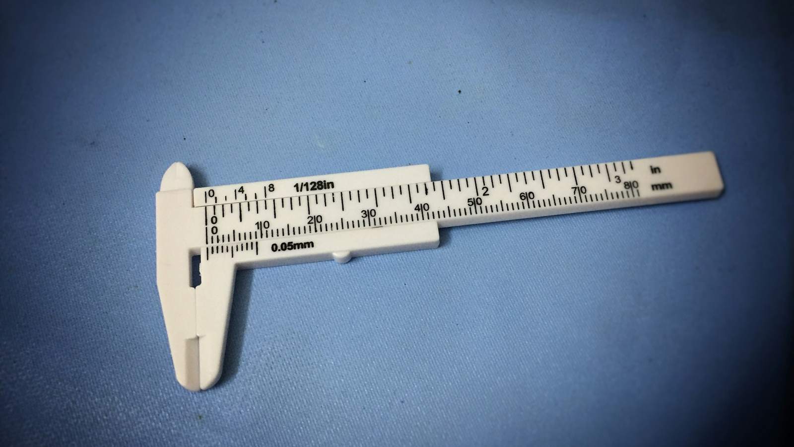 A white plastic vernier caliper on a blue surface, representing measuring each shipment against the agreed specification