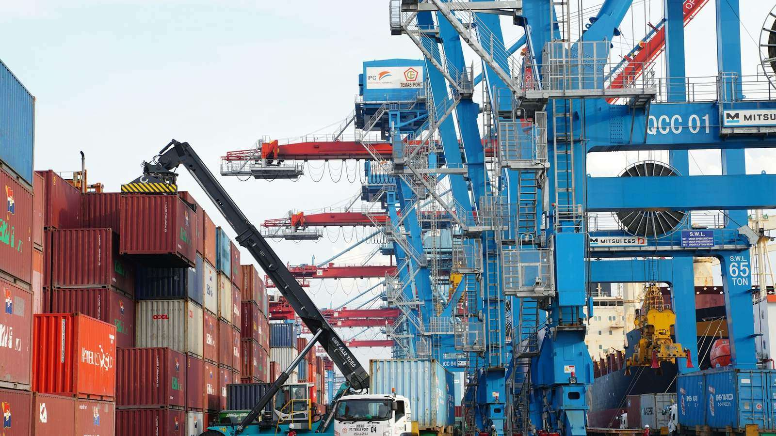 Quay cranes and a stack of containers at a working terminal with a vessel alongside, representing the transhipment leg of a shipment