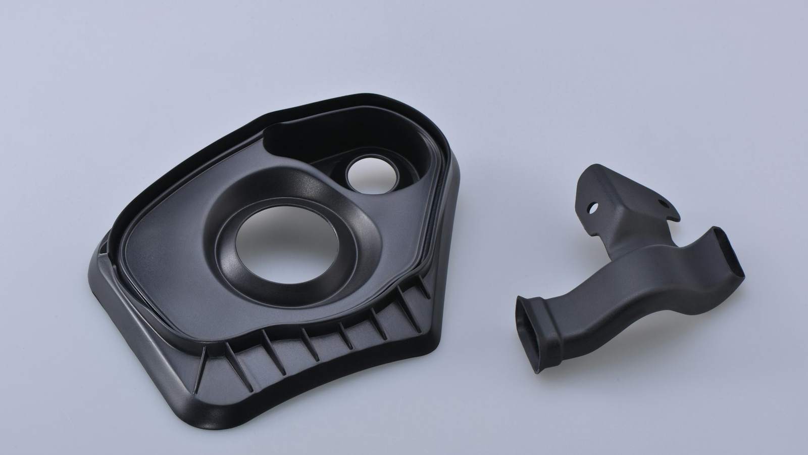 Two custom black injection-moulded plastic parts on a plain background, representing components produced from a buyer's own tooling